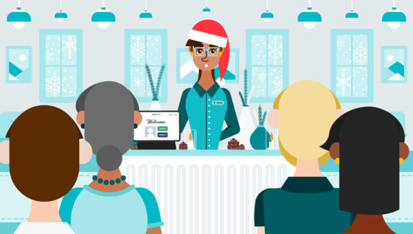 Front desk concierge in a Santa hat greeting visitors in a senior living community decorated for the holidays, with an Accushield visitor management kiosk displayed on the counter.